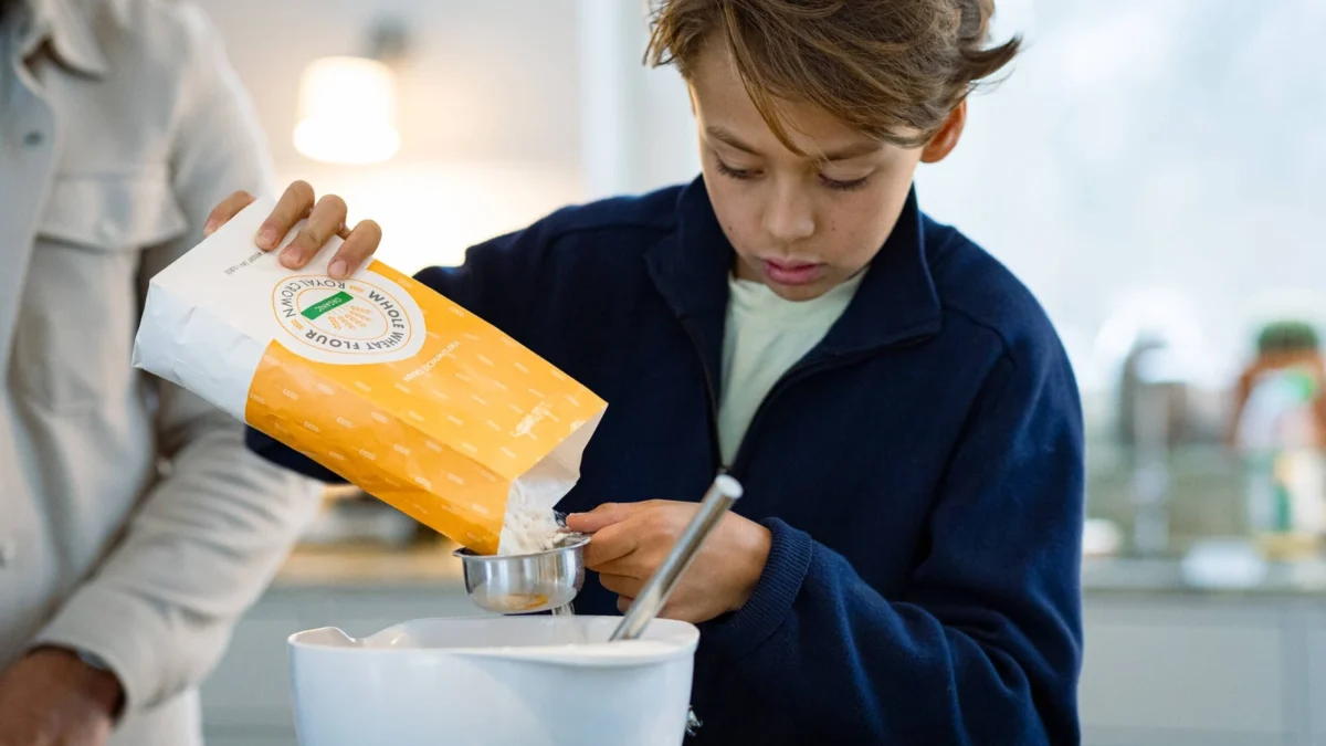 A paper flour bag being used to pour flour into a measuring cup