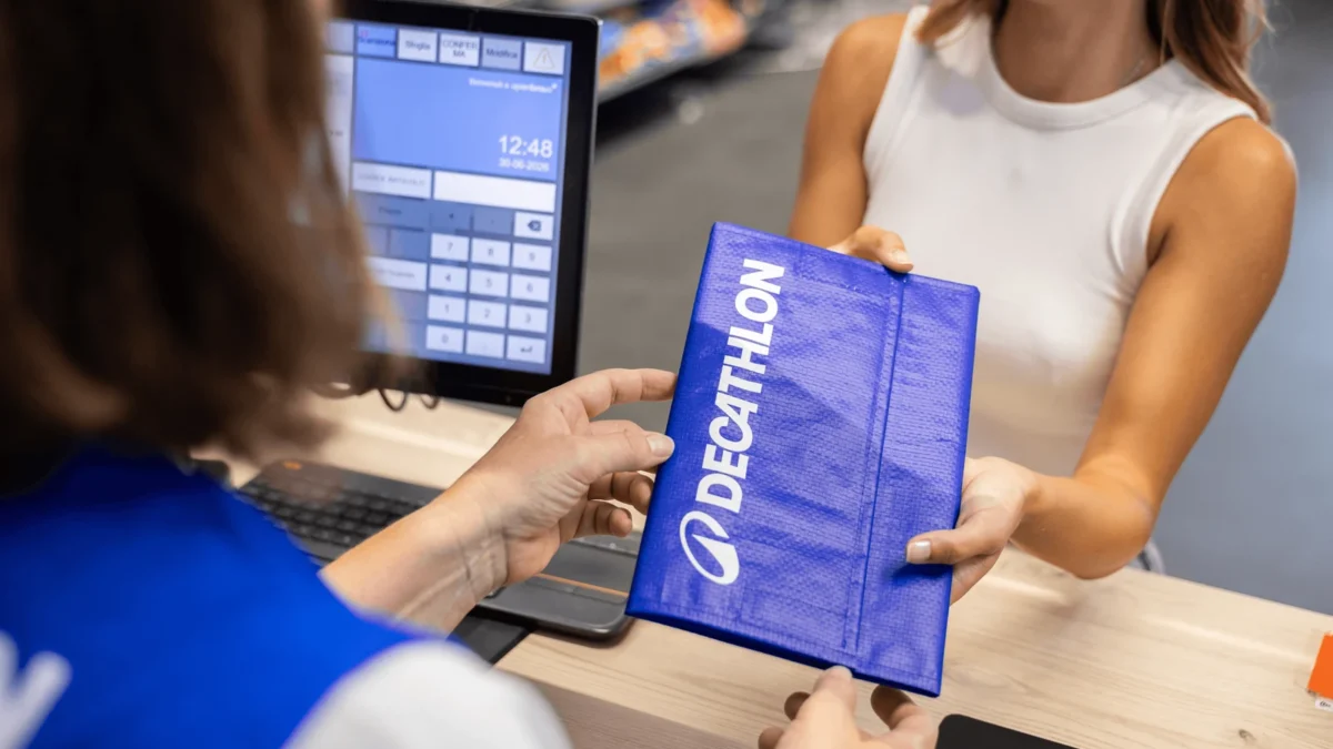 A blue Decathlon-branded reusable parcel being handed across a retail counter.