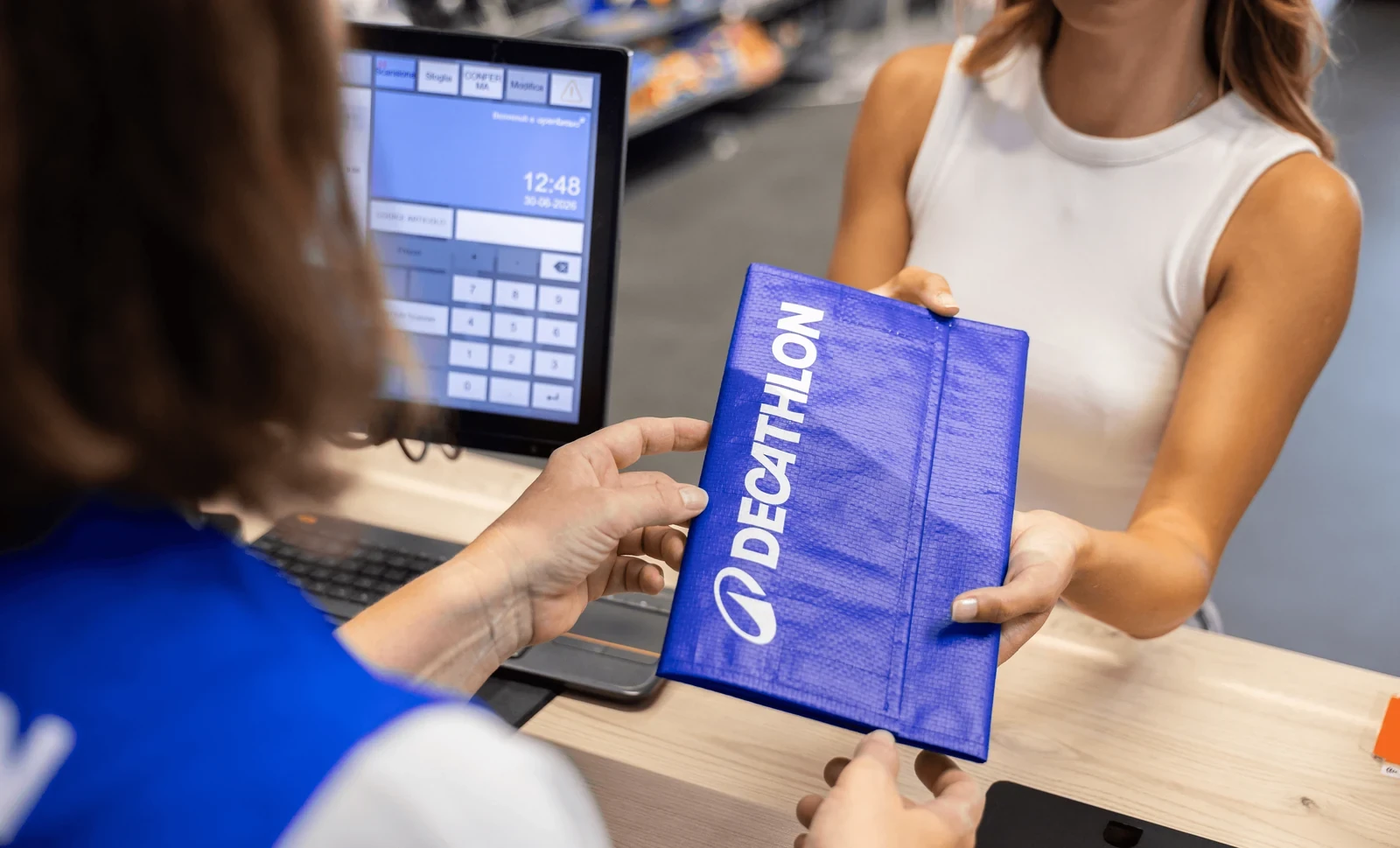 A blue Decathlon-branded reusable parcel being handed across a retail counter.
