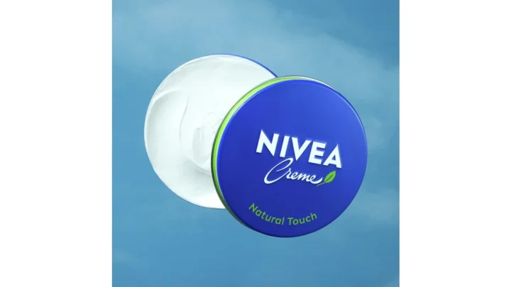 An open NIVEA Creme Natural Touch tin with a blue and green lid against a blue background.