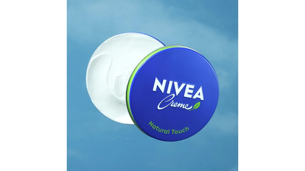 An open NIVEA Creme Natural Touch tin with a blue and green lid against a blue background.