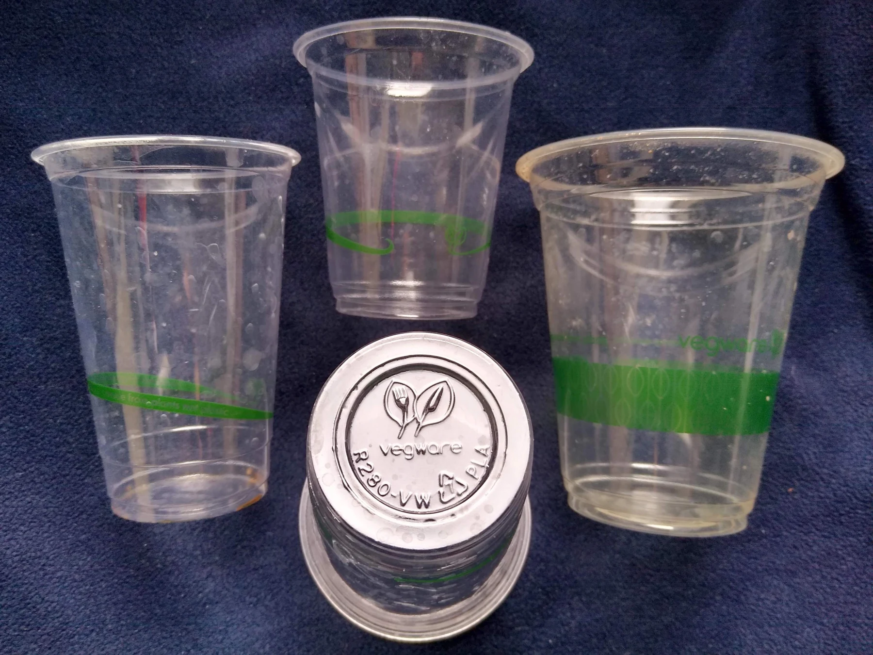 Four clear PLA cups, including one inverted to show its marked base; no PHA or PBAT samples are pictured.