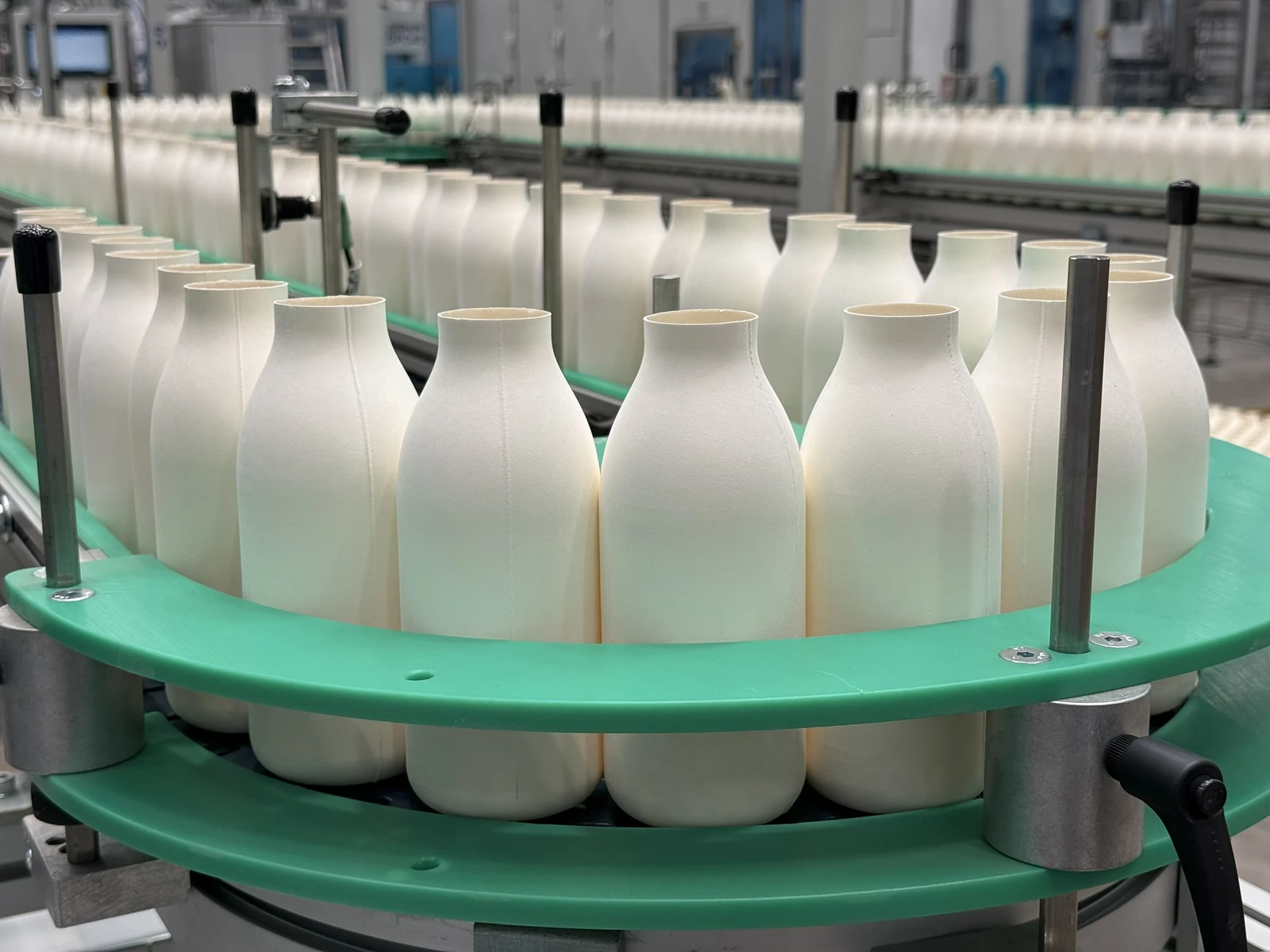 Unfilled fibre bottle bodies on a green industrial conveyor in the Pulpex announcement photograph.
